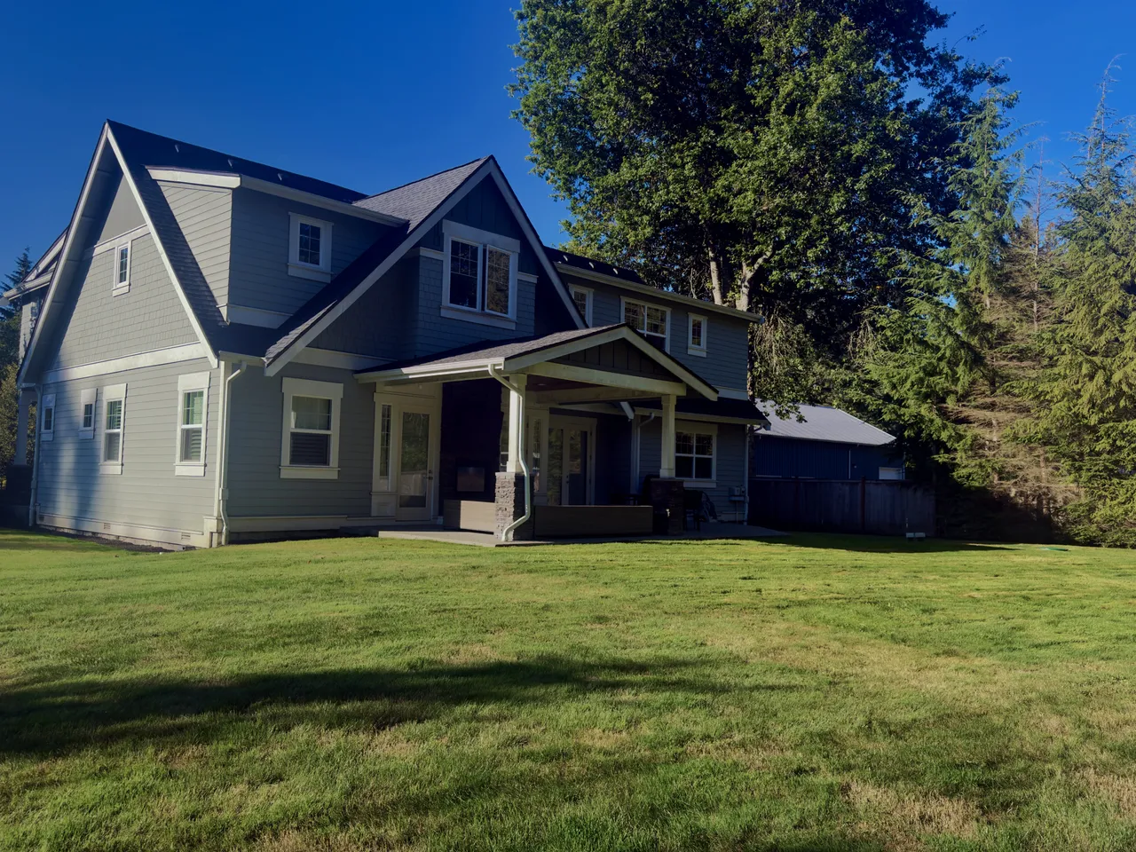 Grey craftsman house behind a wide freshly cut lawn under evergreens