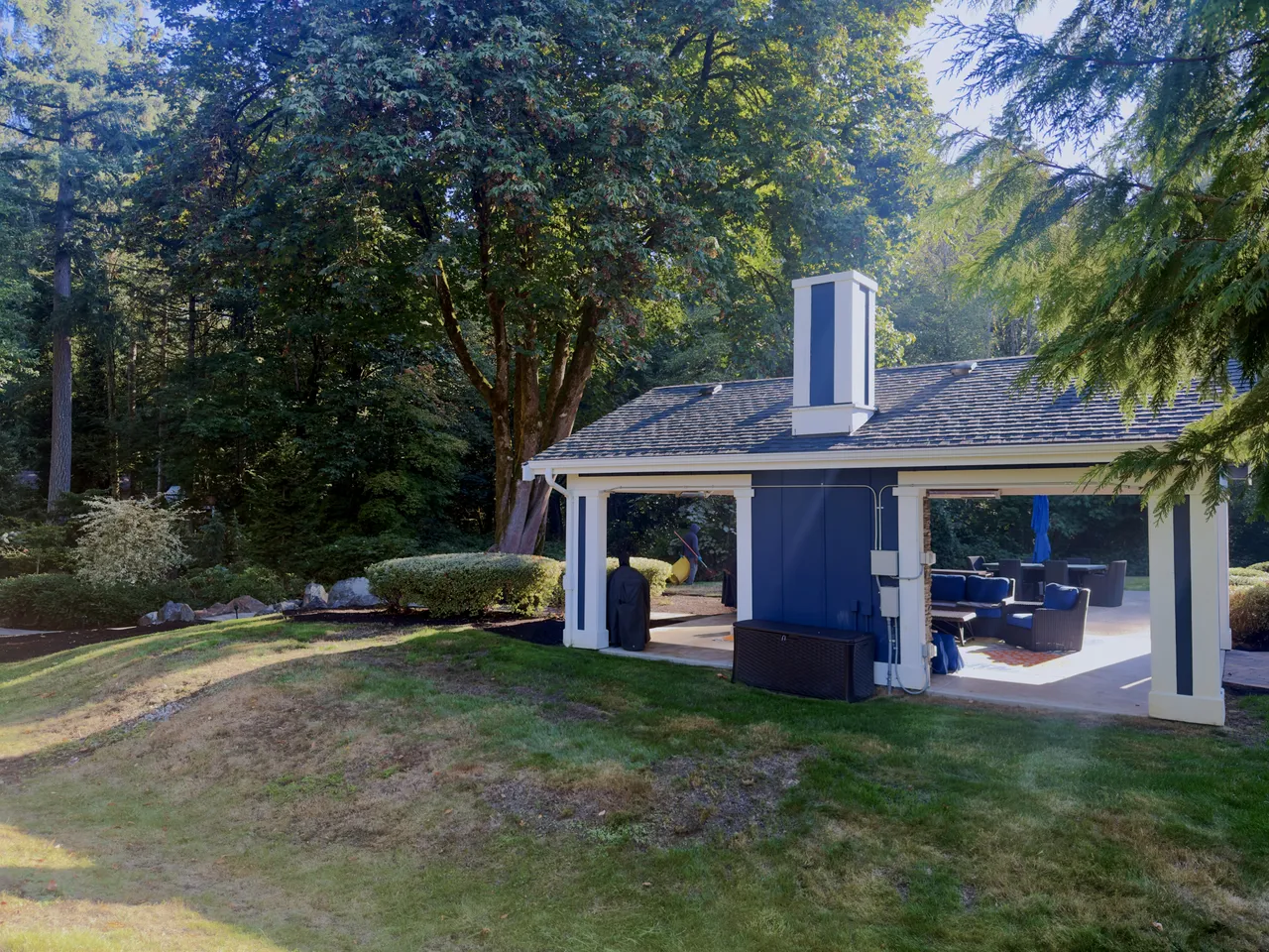 Backyard pavilion and lawn surrounded by tall evergreens