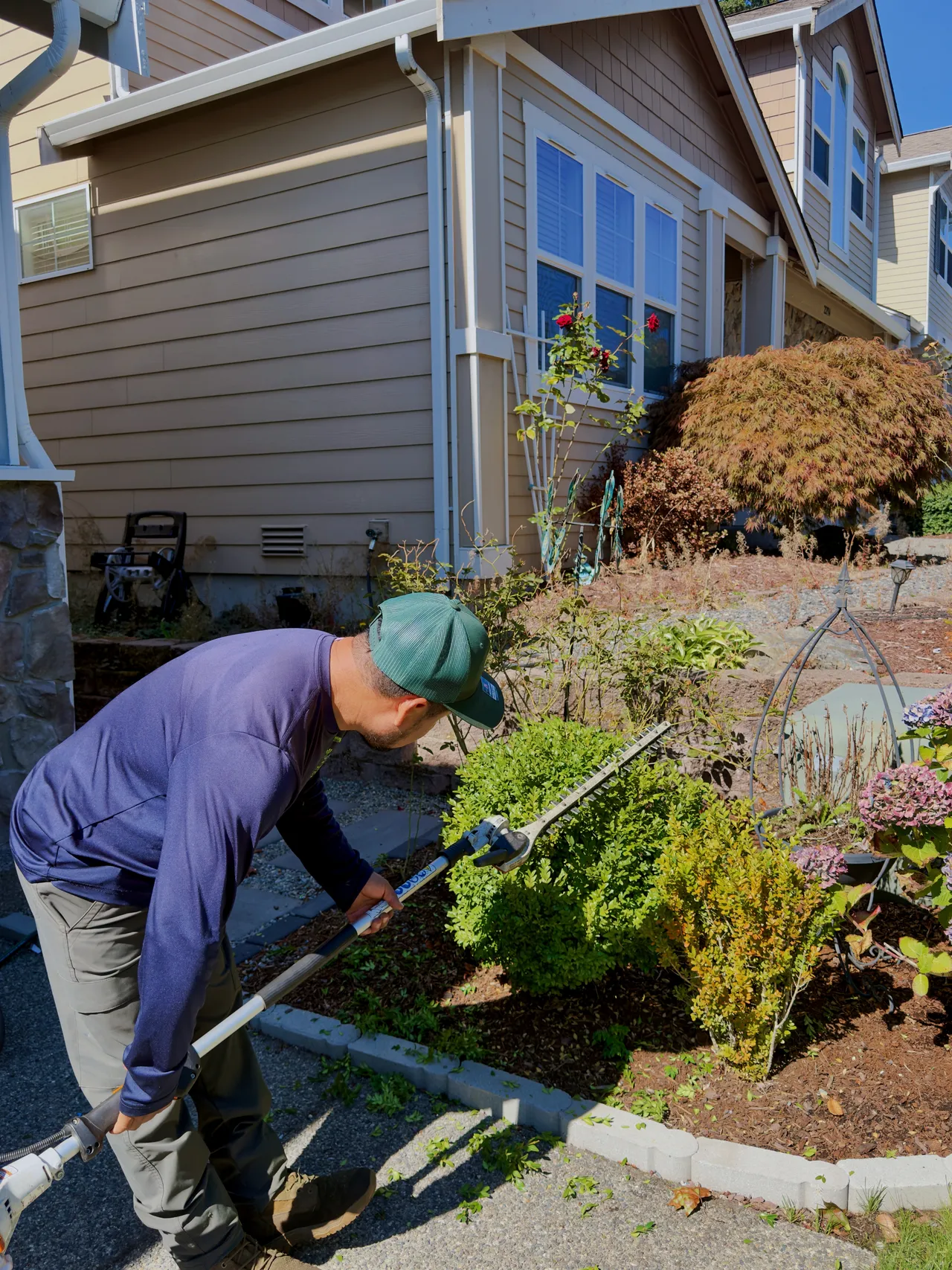 A crew member trims the foundation shrubs below the window