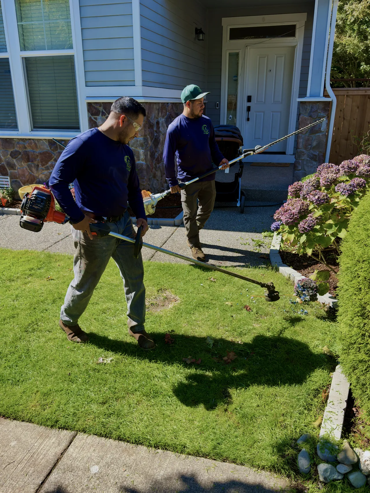 Two crew members working the front beds with a trimmer and a blower