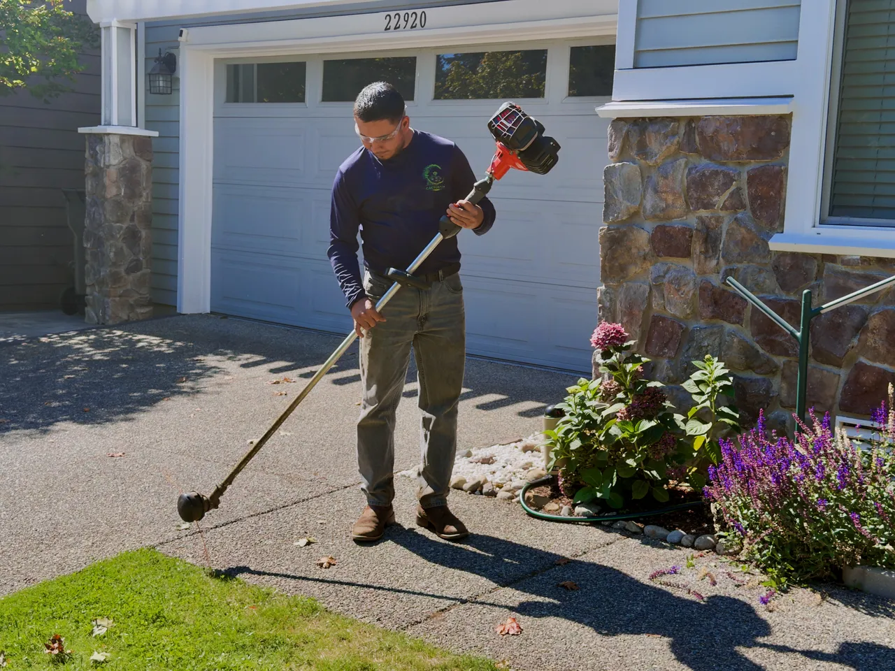 A crew member string trims the edge of the drive by the garage