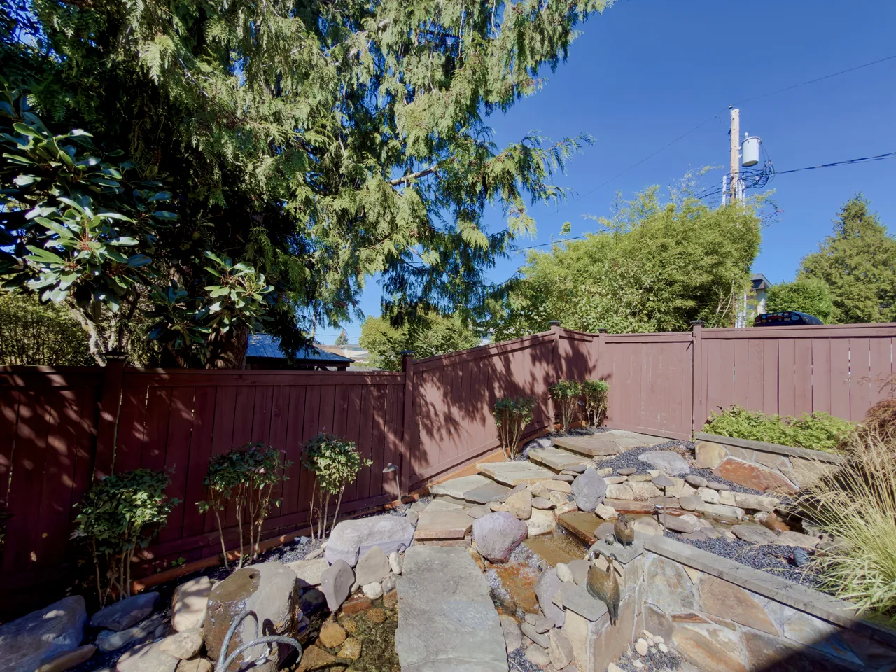 Dry stack stone retaining wall under construction beside a cedar fence