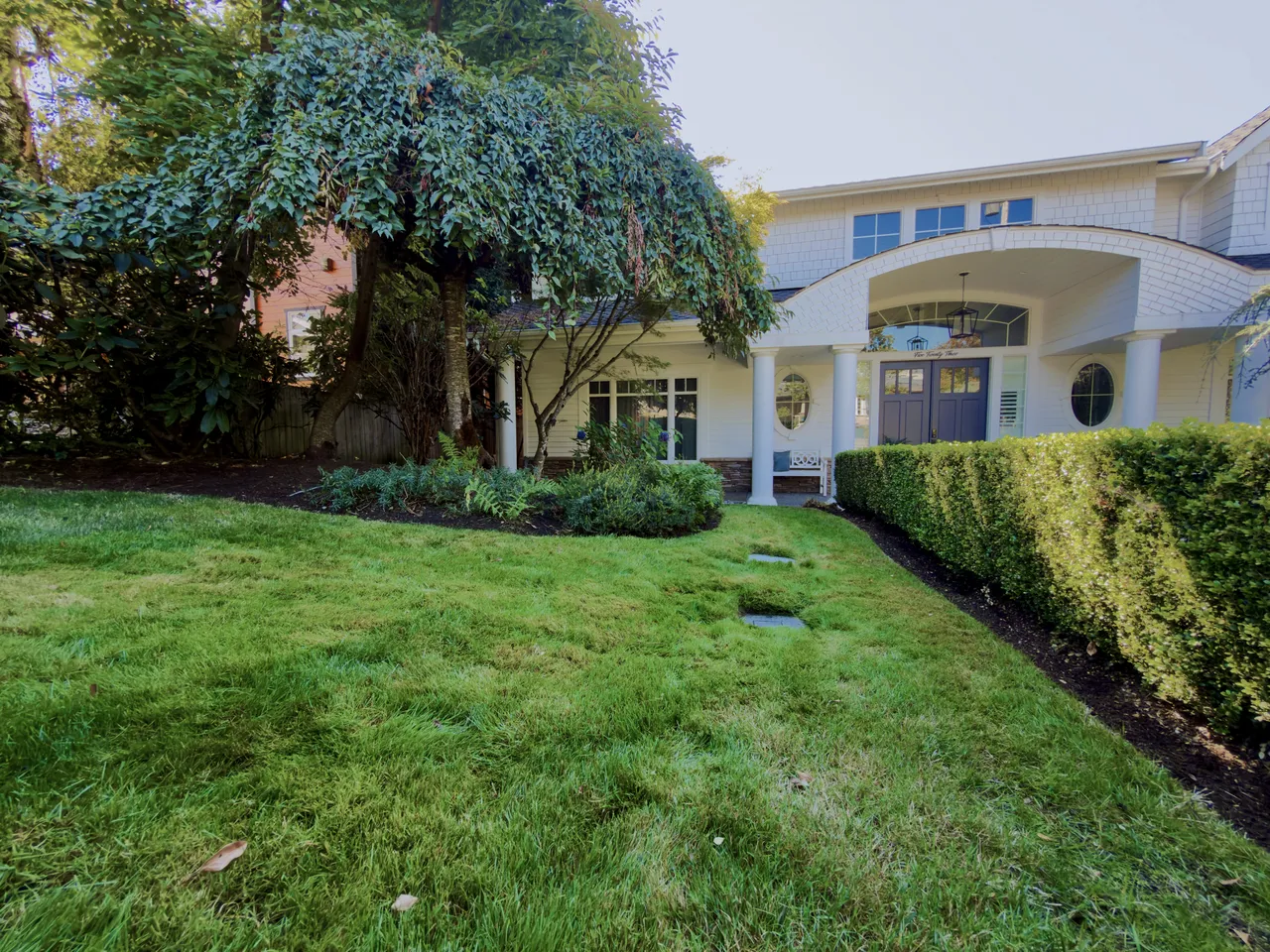 White colonial house with a hedge line and cut lawn