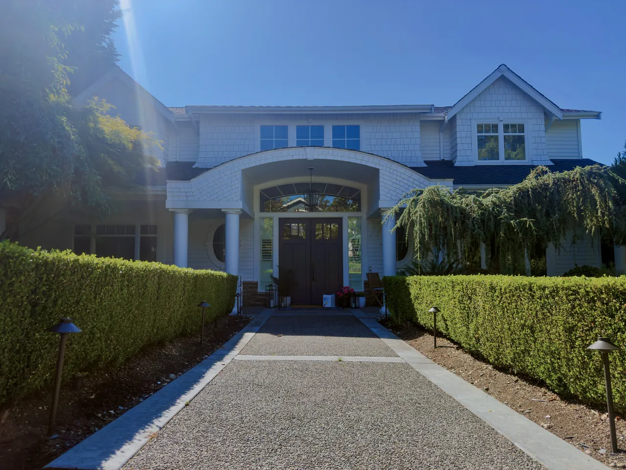 Trimmed boxwood hedges lining a gravel walk to a white colonial house