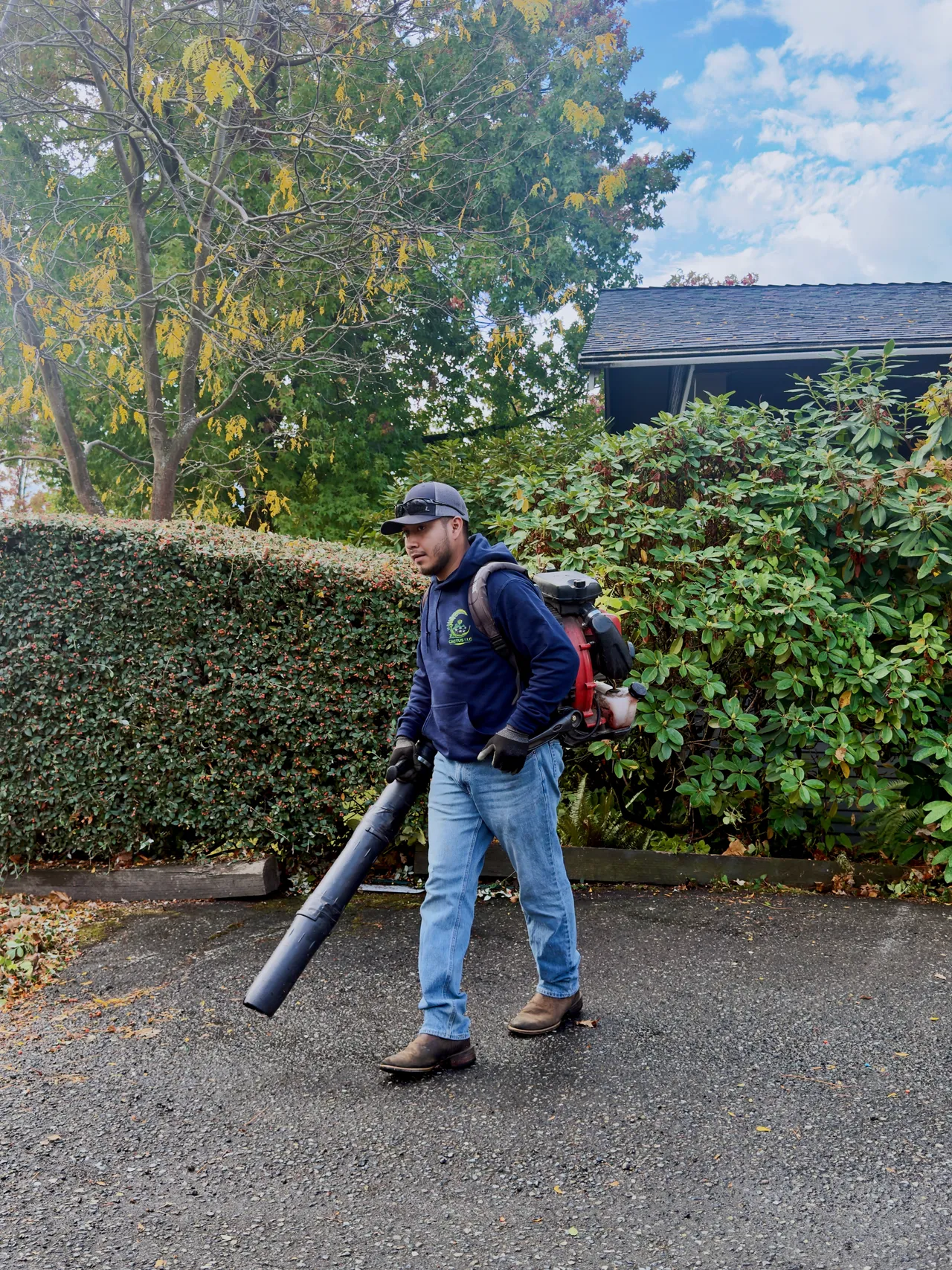 A crew member walks the drive with a backpack blower, leaves cleared to the edge