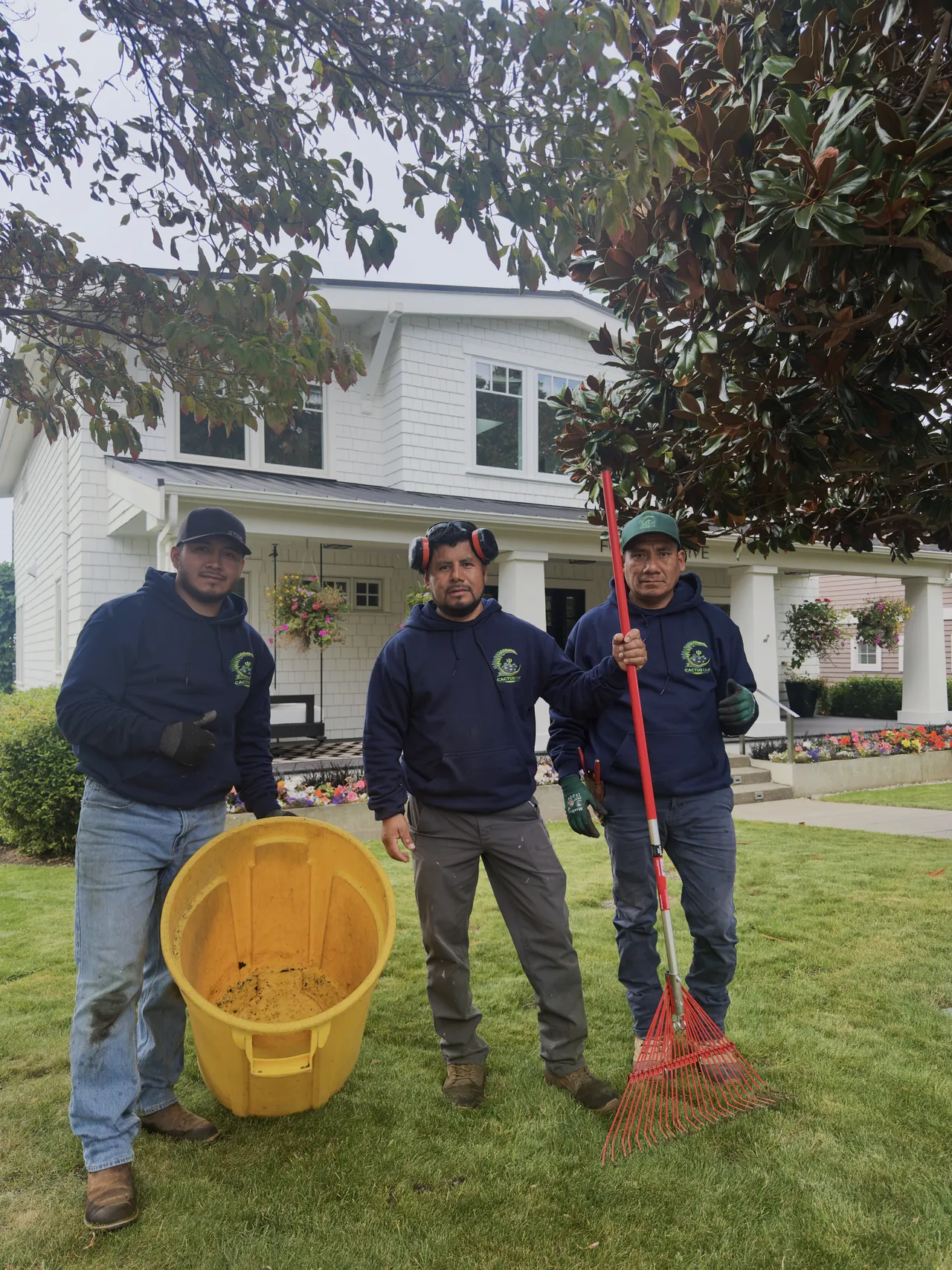Three crew members with a rake and bucket in front of a white house
